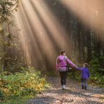 Mother and daughter walking in forest with sunbeams shining over them